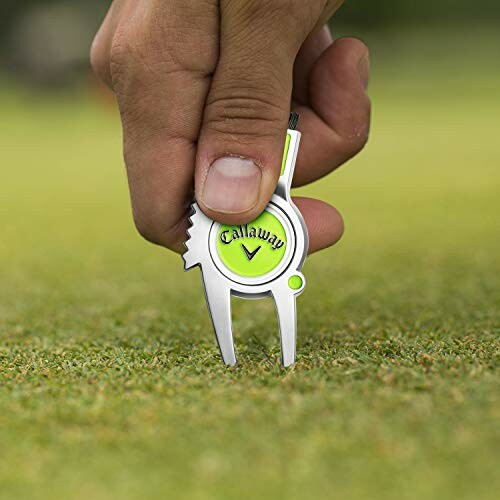 Hand using Callaway golf divot tool on grass